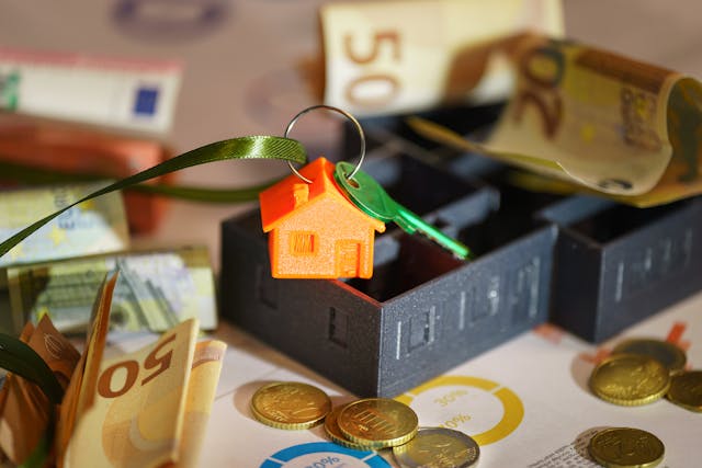 a green key tied to a keychain with a little orange house surrounded by money