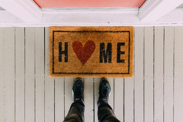 a doormat on a front door that says "home" with the "o" being shaped like a heart